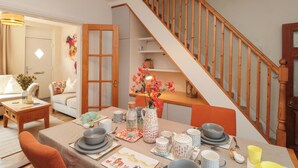 A dining area with a table set for four, a staircase, and a door leading to another room. - Moot Cottage (Driffield)
