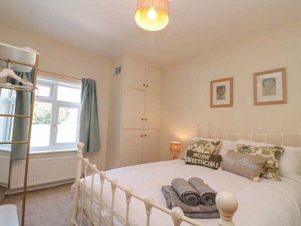 A bedroom with a bed, a wardrobe, a radiator, a window with a curtain, and a hanging light fixture. - Moot Cottage (Driffield)