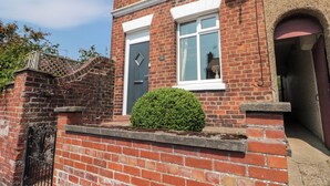 A two-story brick house with a white door and windows, a small garden, and a satellite dish. - Moot Cottage (Driffield)