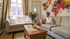 A living room with two sofas, a wooden coffee table, a vase with flowers, and a colorful abstract wall painting. - Moot Cottage (Driffield)