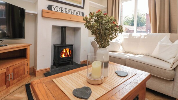 A cozy living room with a fireplace, a television, a sofa, and a table with a vase of flowers. - Moot Cottage (Driffield)
