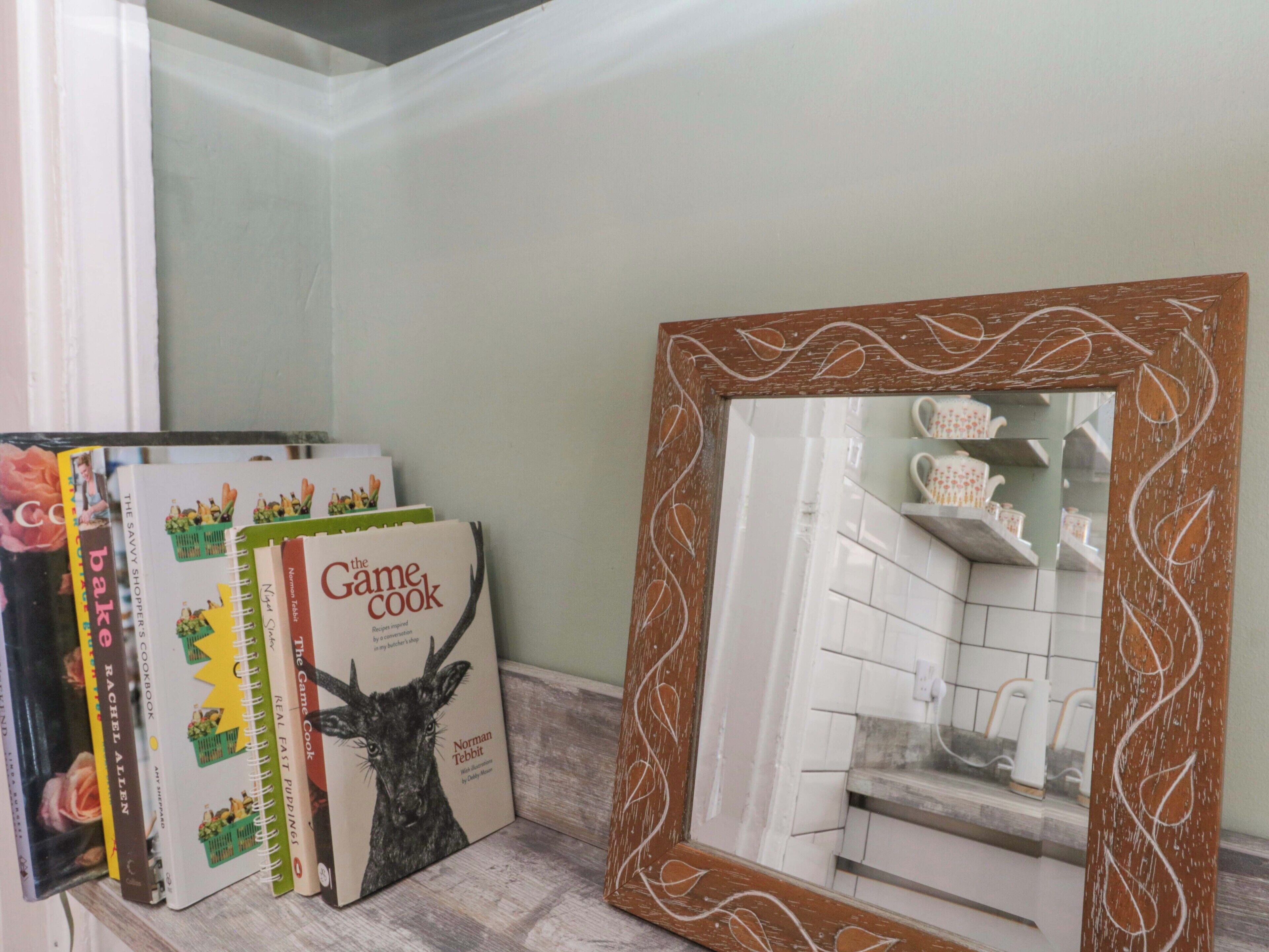 Una cocina con encimera blanca, espejo con marco decorativo y varios libros de cocina.