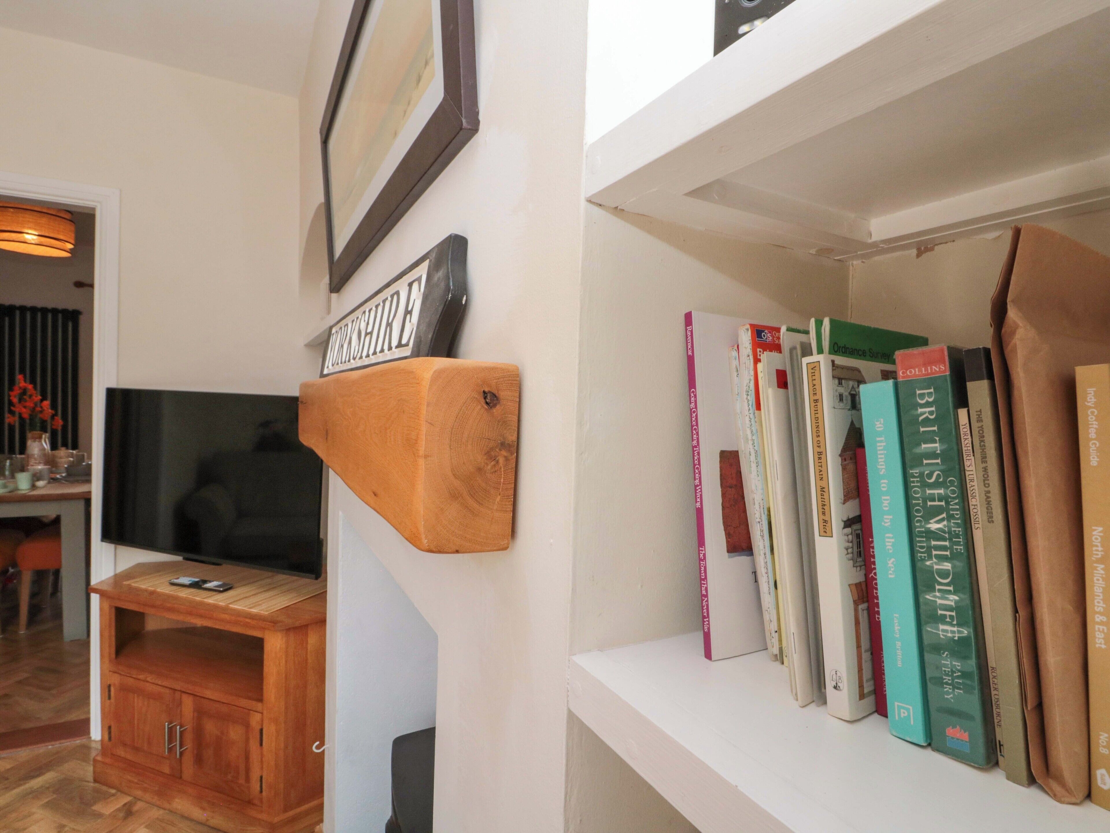 A living room with a mounted wooden sign reading "Yorkshire," a television, a wooden cabinet, and a bookshelf with various books.