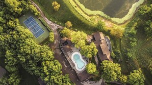 Vista aérea de una propiedad con cancha de tenis, piscina y jardín ajardinado.