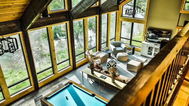 Una habitación amplia con ventanas grandes, una mesa de billar y una zona de estar con sofás y una mesa de centro.