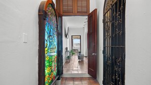 Un couloir étroit au sol carrelé, une porte en vitrail aux couleurs vives et un portail en métal.