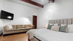 Une chambre à coucher comprenant un lit, un canapé, un téléviseur fixé au mur et une table de chevet avec une lampe.