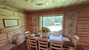 L’intérieur d’un chalet en bois comprend une table à manger, quatre chaises, un vase de fleurs et une citation encadrée accrochée au mur.