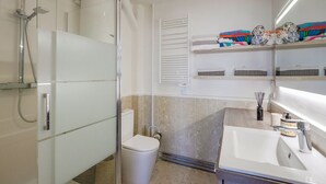 A modern bathroom with a glass shower enclosure, a toilet, a sink with a mirror, and shelves with towels and toiletries. - Cosy studio with terrace overlooking Marseille (Marseille)