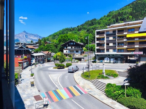 Vista de una calle con una farmacia, un edificio con balcones y una montaña al fondo.