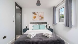 A modern bedroom with a bed, two bedside tables, a window with curtains, and artwork on the wall.