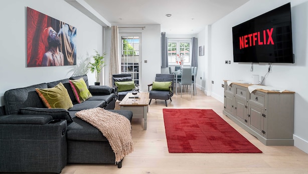 A modern living room with a grey sofa, red rug, and a TV displaying "NETFLIX".