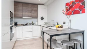 A modern kitchen with white cabinets, a wooden countertop, and a dining area with a table and bar stools.