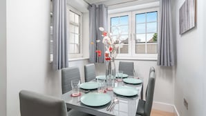 A dining area with a rectangular table set for four, grey curtains, and a vase with flowers.