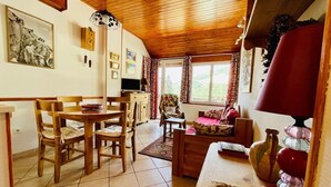 A cozy living room with a wooden ceiling, a dining area with wooden chairs and a table, and a sofa with a red cushion. - Apartment for 4 with with nice view of Briançon (Briançon)