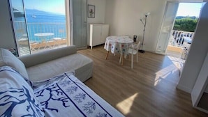 A modern room with a large sliding glass door to a balcony, a sofa, a small round table with a floral tablecloth, and a view of the sea. - Beautiful 41 m² with balcony (Antibes)