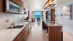 Une cuisine moderne dotée d’un îlot central, d’appareils électroménagers en acier inoxydable et offrant une vue sur la mer.