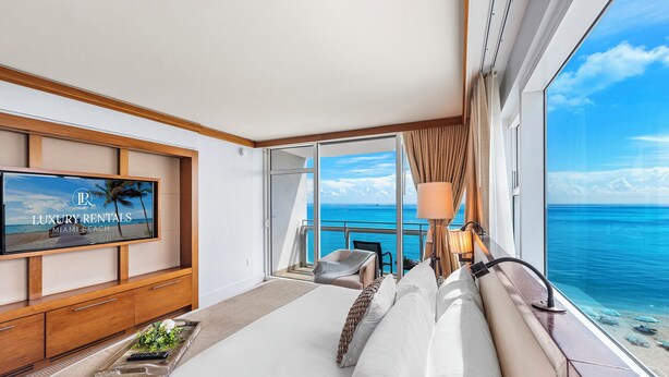 Une chambre à coucher luxueuse, dotée d’un grand lit, d’une télévision et offrant une vue sur l’océan.