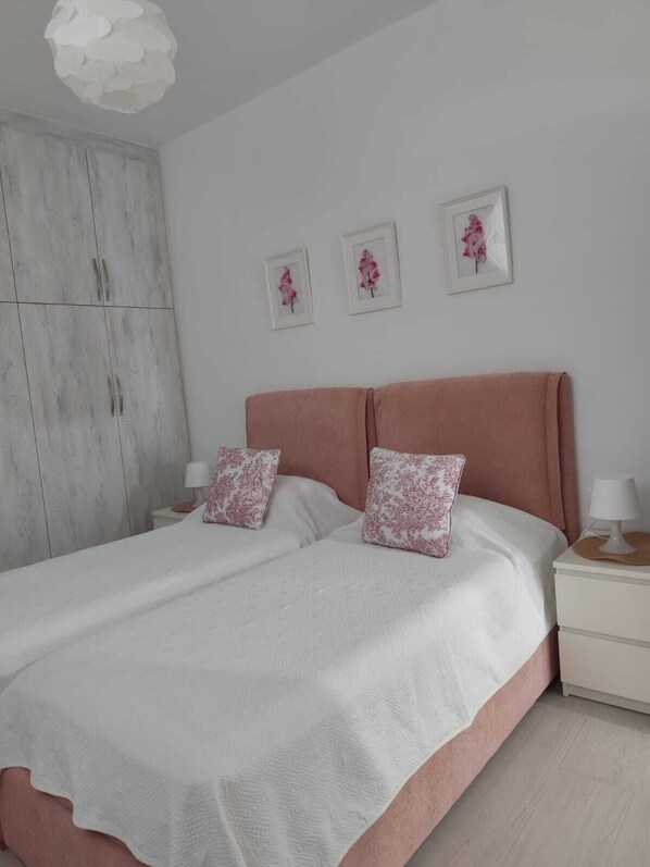 A bedroom with a bed, two nightstands, a wardrobe, and three framed pictures on the wall.