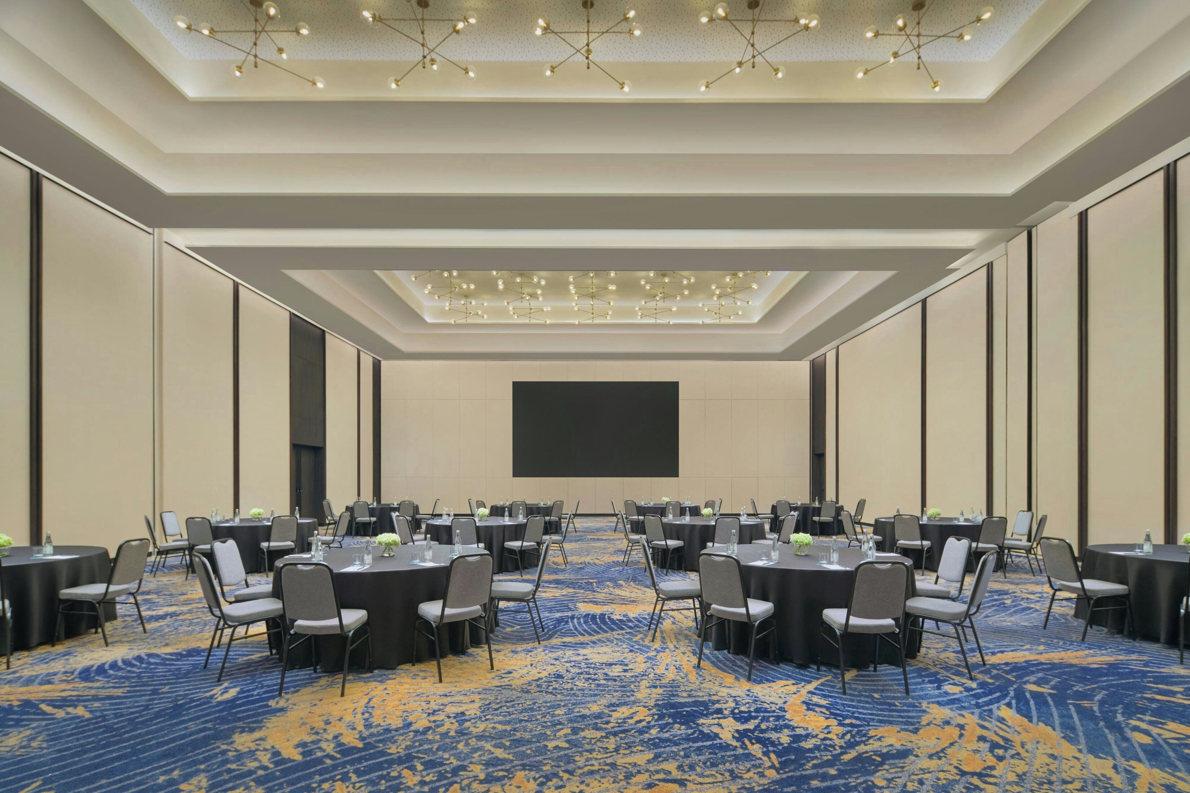 A conference room with a large screen, round tables, and chairs arranged for a meeting.