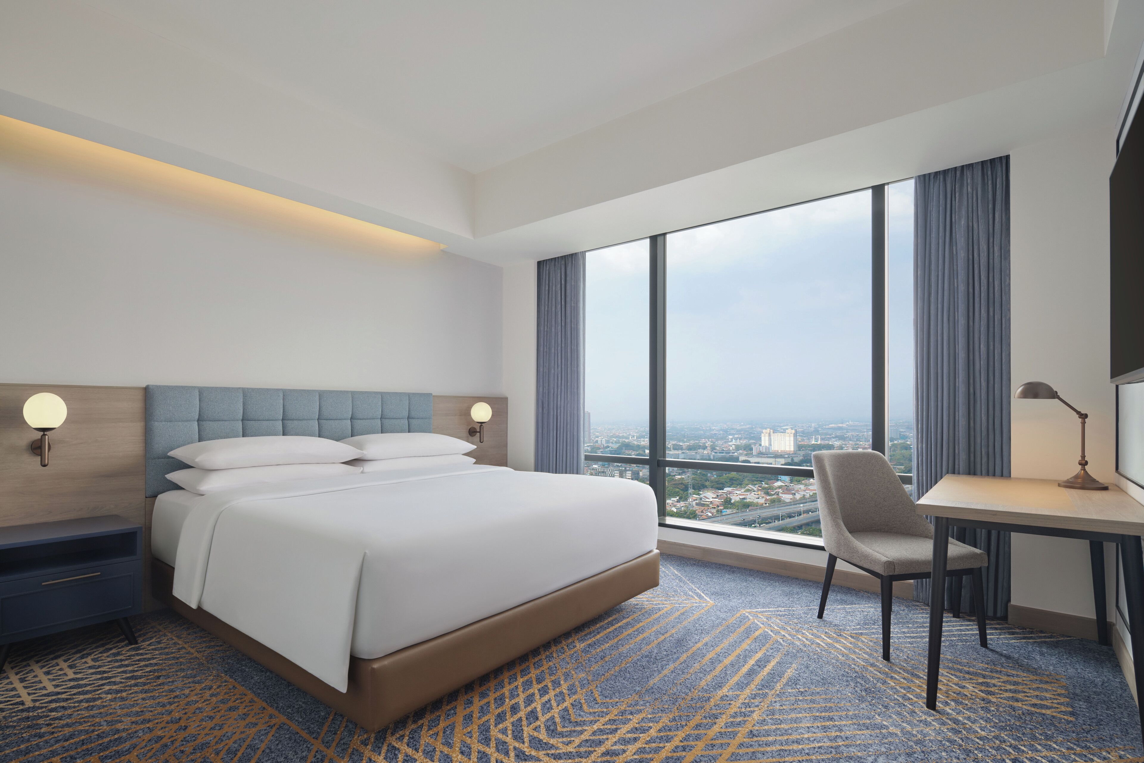 Ein modernes Hotelzimmer mit einem großen Bett, einem Schreibtisch und Blick auf die Stadt.
