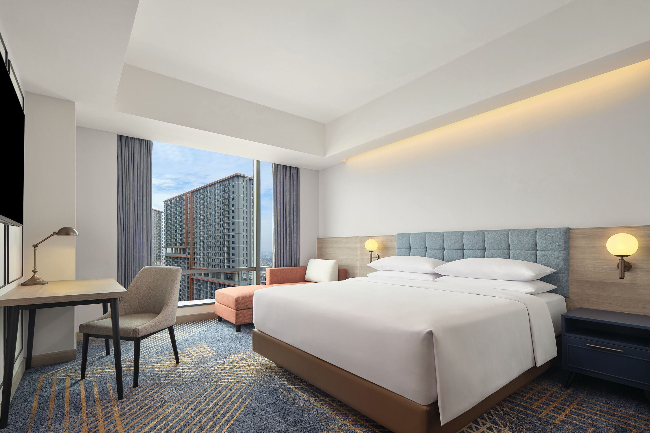Habitación de hotel con una cama grande, un escritorio, una silla y vistas a edificios altos.