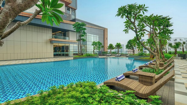 A modern hotel with a swimming pool, lounge chairs, and lush greenery. - Four Points By Sheraton Bekasi (Bekasi)
