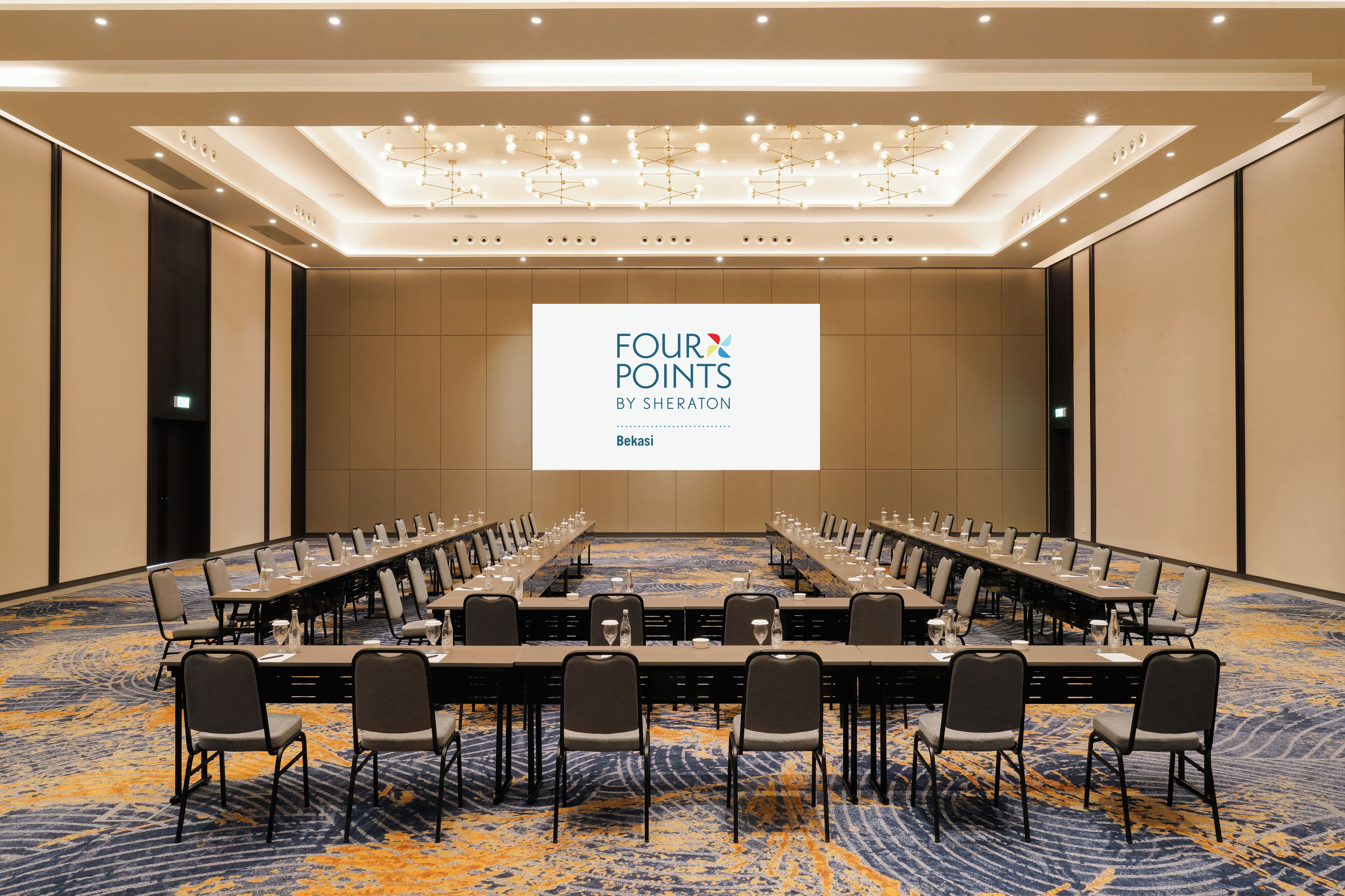 A conference room with a long table and chairs, a large screen displaying text, and a carpeted floor.