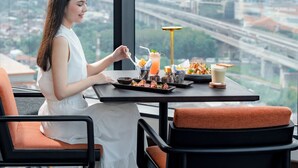 A woman dining at a table with a city view, a glass of orange drink, and a plate of food. - Four Points By Sheraton Bekasi (Bekasi)