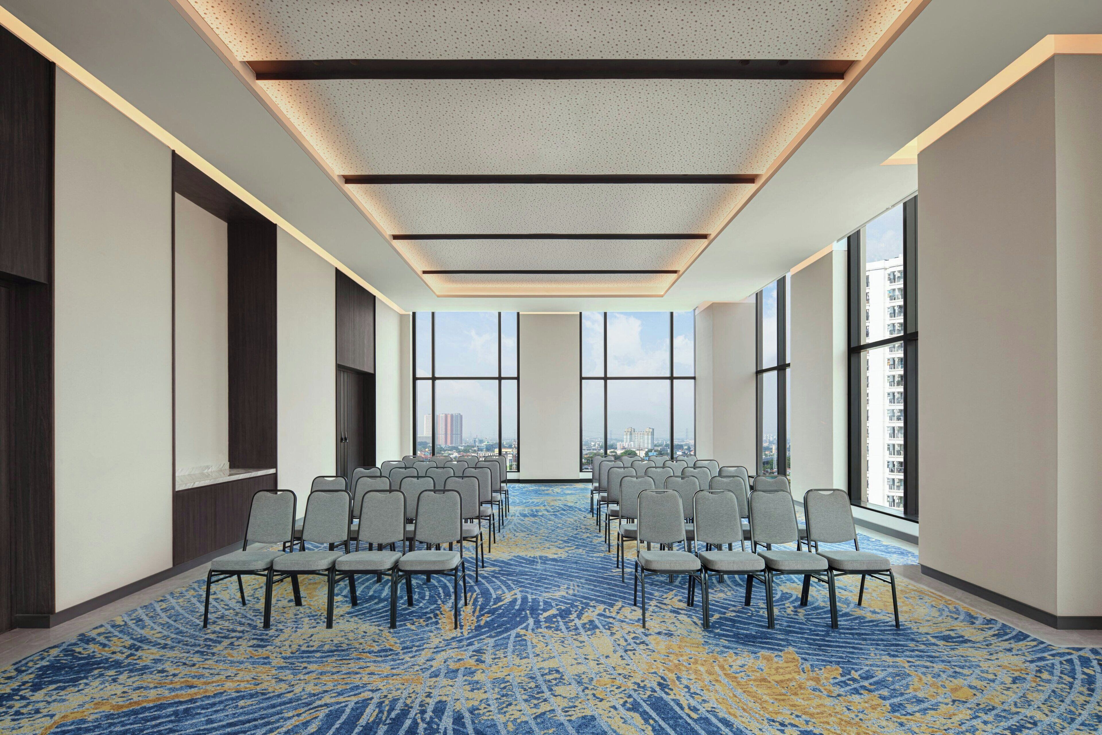 A conference room with rows of chairs, large windows, and a patterned carpet.