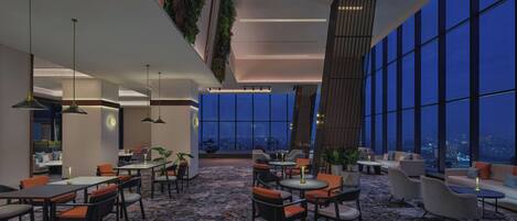 A modern hotel lobby with high ceilings, large windows, and a mix of seating areas including tables and sofas.