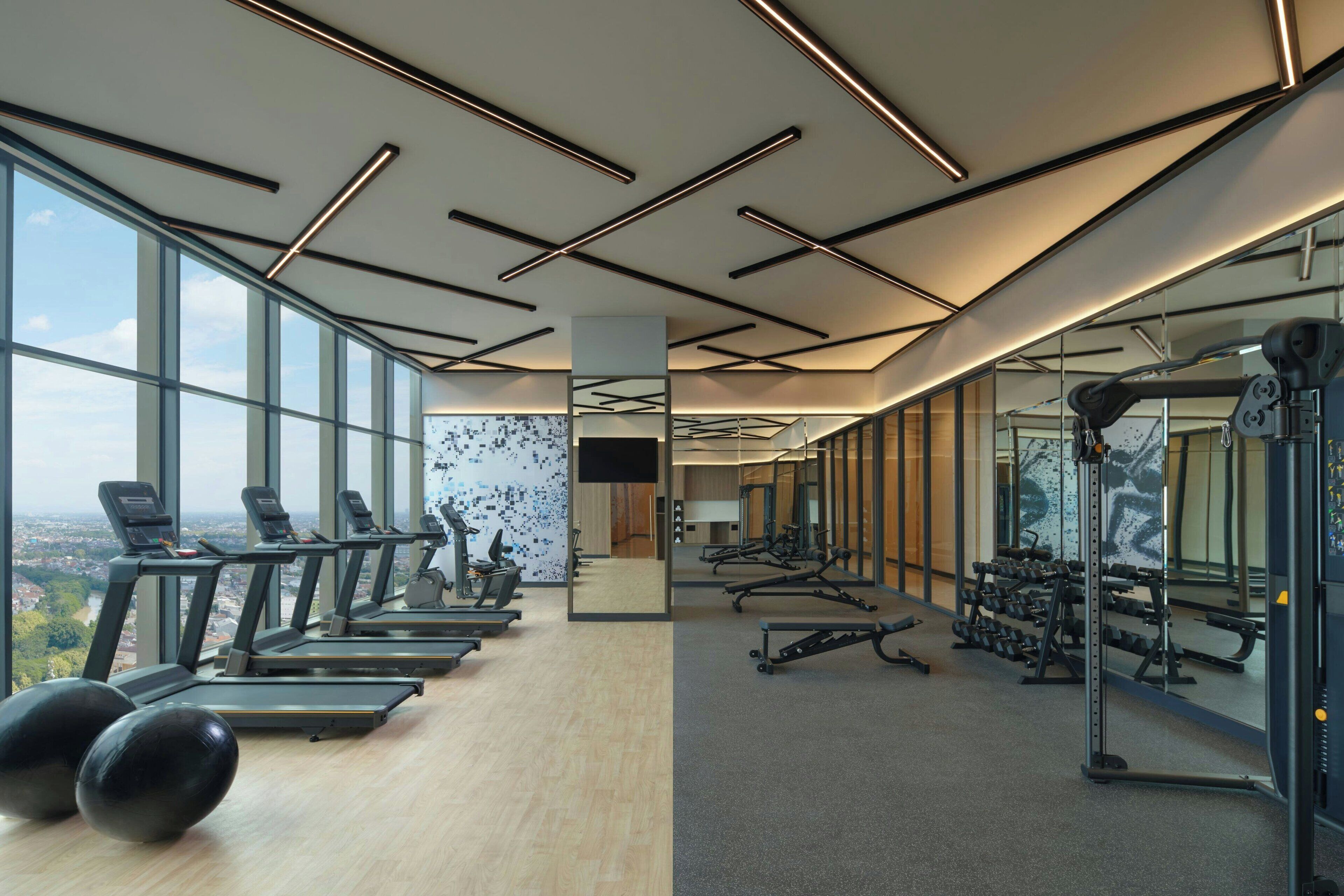 Une salle de sport moderne équipée de tapis de course, de poids et d’appareils d’exercice. De grandes fenêtres offrent une vue sur la ville.