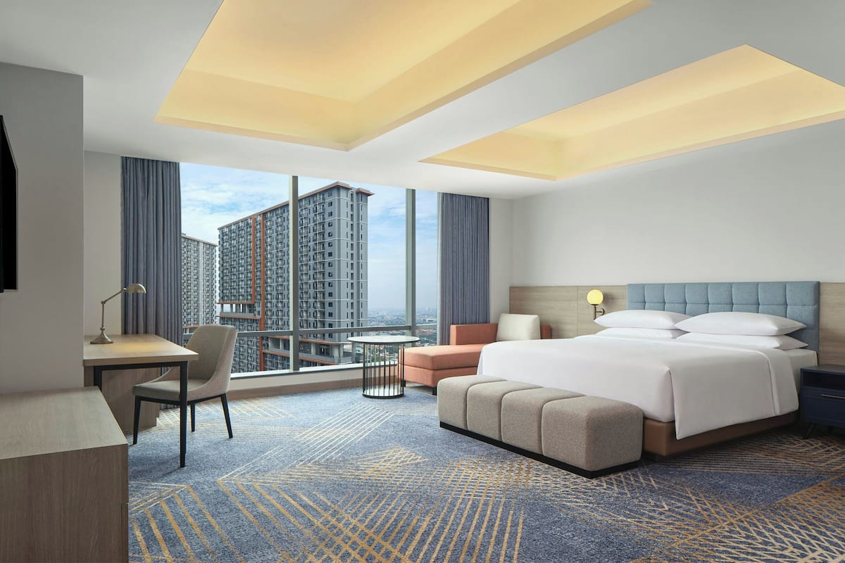 Une chambre d’hôtel avec un grand lit, un bureau, une chaise, une petite table et une vue sur des immeubles de grande hauteur.