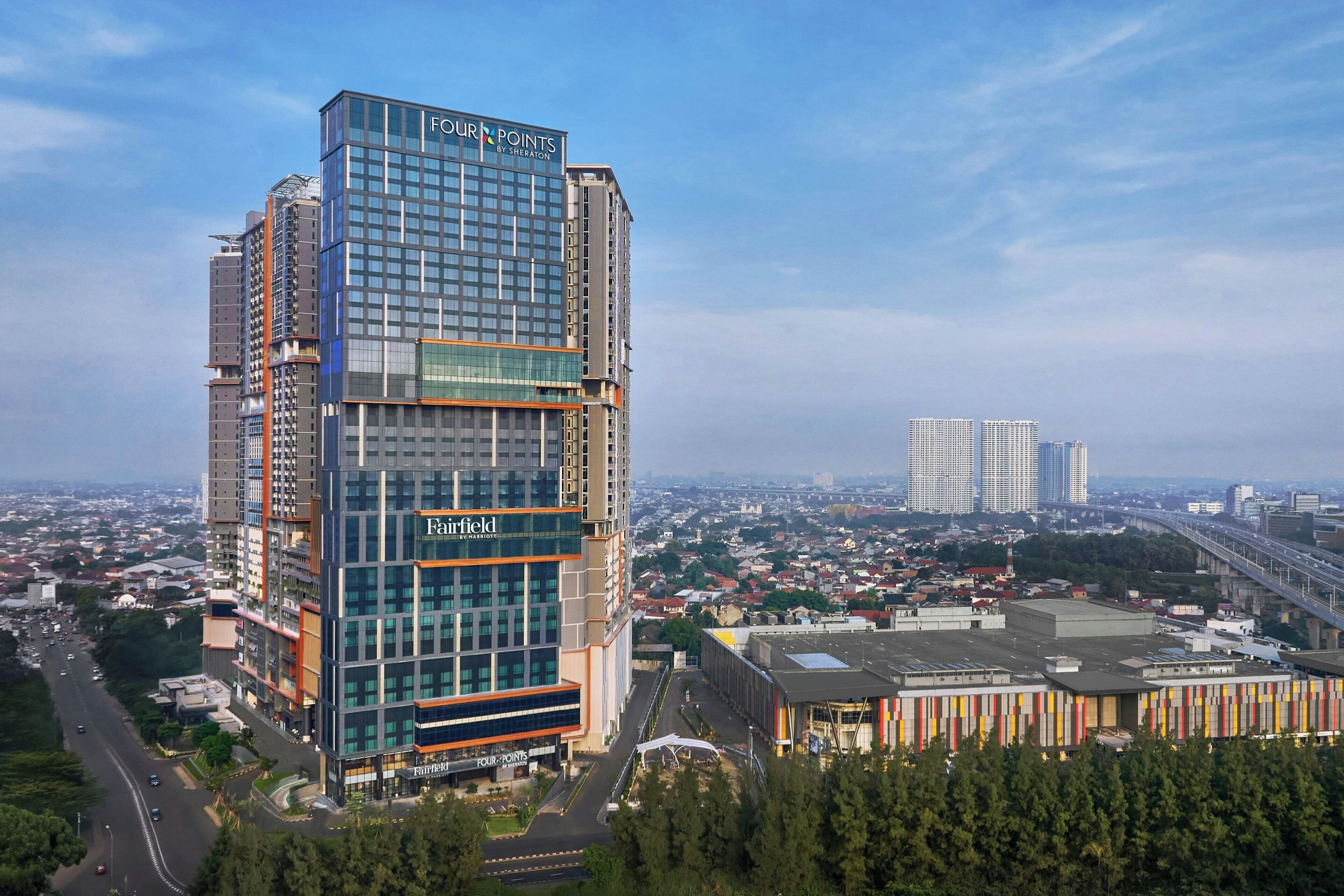 Un hôtel à plusieurs étages doté d’une façade en verre, nommé « Fairfield by Marriott », et surmonté d’une grande enseigne « Four Points by Sheraton ».