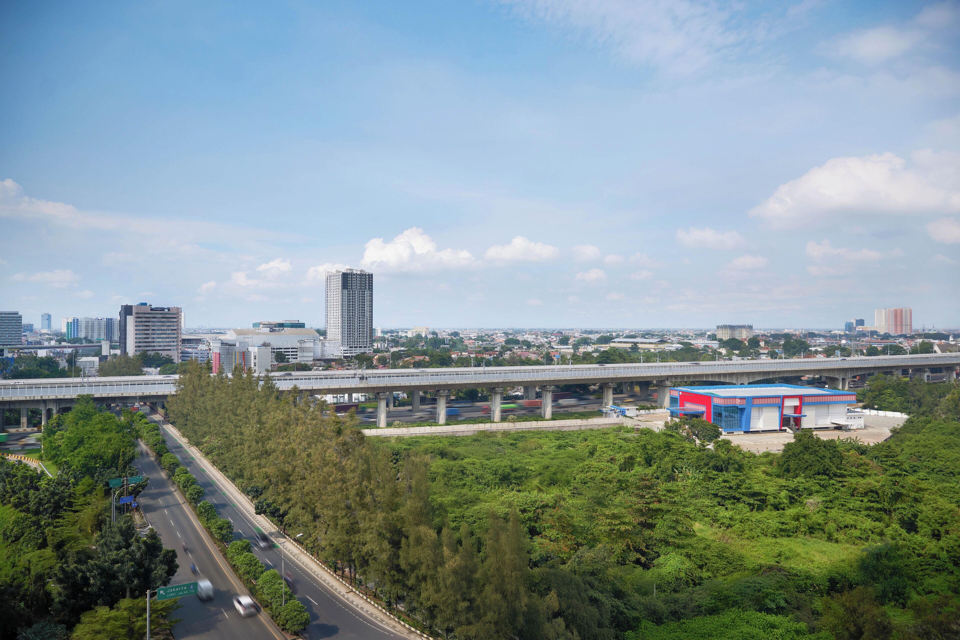 Une autoroute avec un pont enjambant la chaussée, entourée de verdure et avec des bâtiments urbains en arrière-plan.