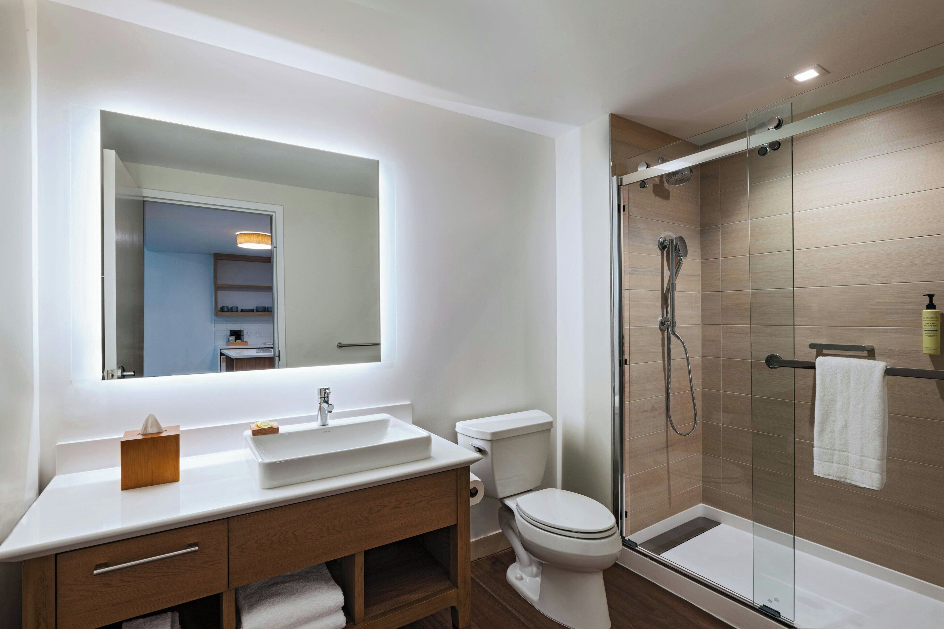 Un baño moderno con un lavamanos blanco, tocador de madera, inodoro y ducha con cerramiento de vidrio.