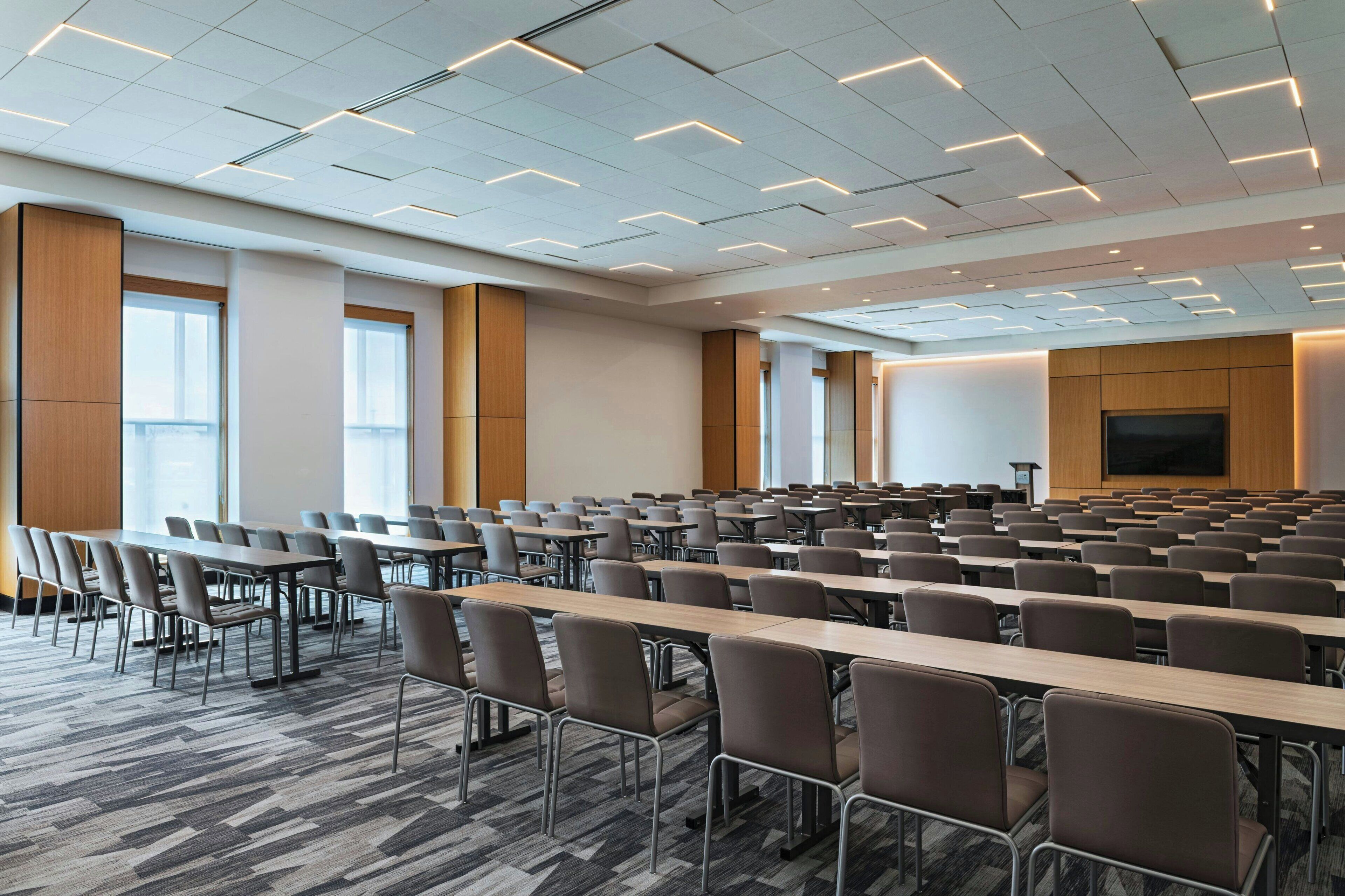 A conference room with rows of tables and chairs, large windows, and a projection screen.