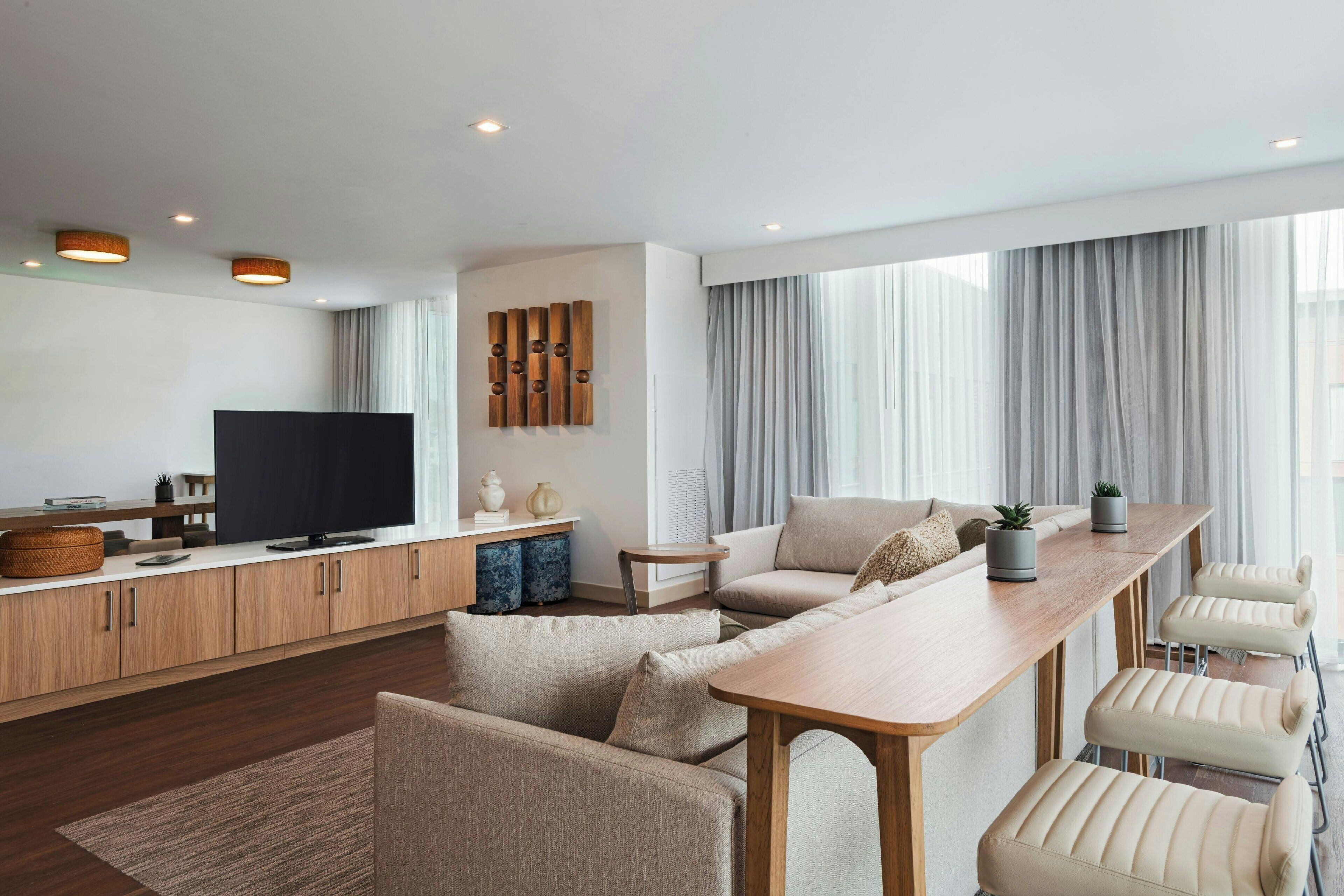 A modern living room with a sofa set, a wooden coffee table, a TV, and a kitchen area with cabinets and a countertop.