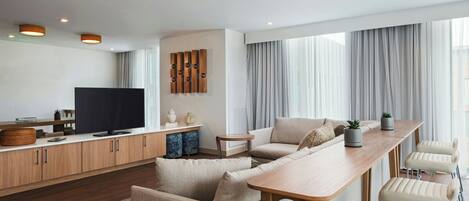 A modern living room with a sofa set, a wooden coffee table, a TV, and a kitchen area with cabinets and a countertop.
