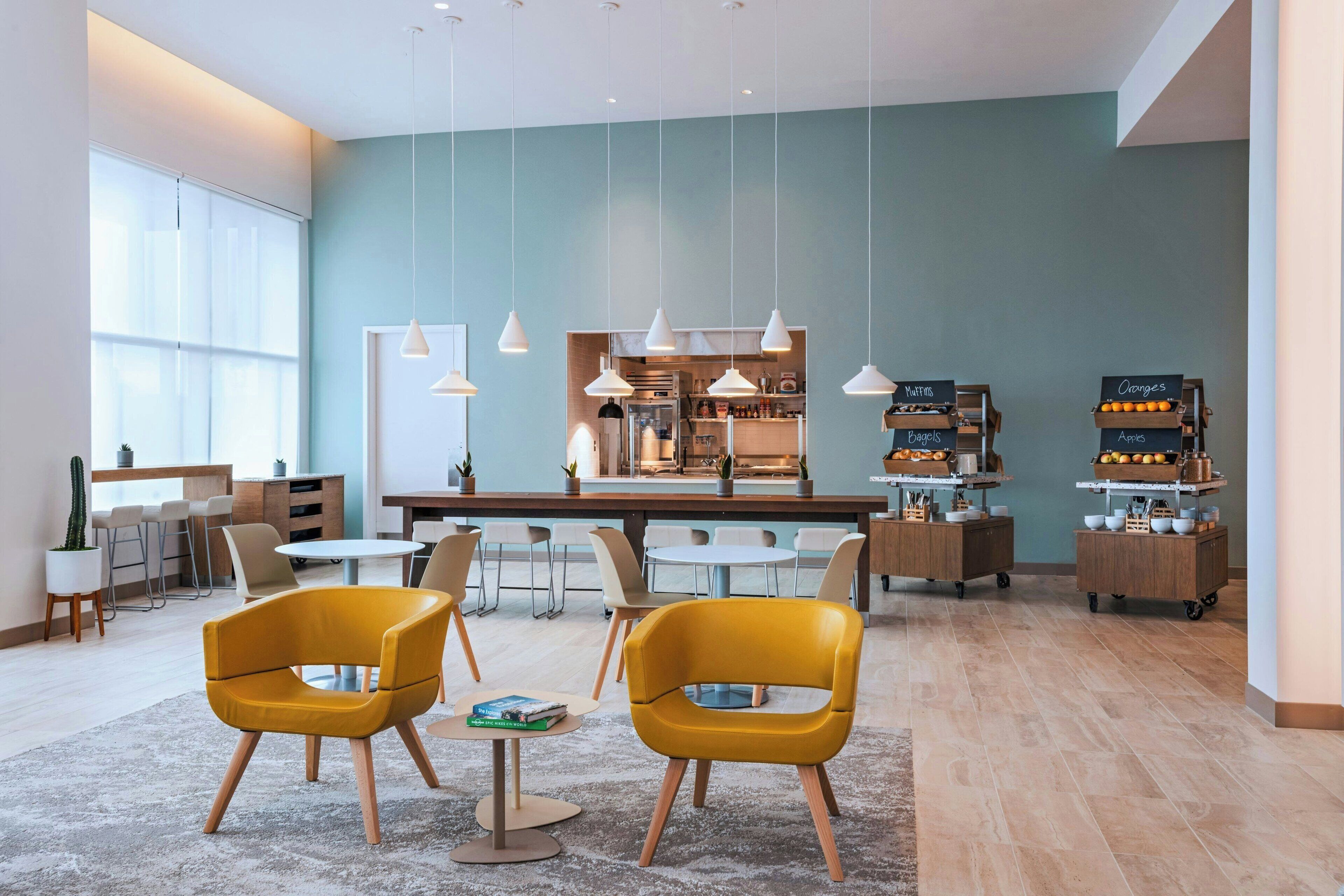 Een modern café met gele stoelen, een keukenhoek en een menubord.