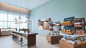 A modern breakfast bar with a wooden counter, white bar stools, and a chalkboard menu displaying 'Oranges' and 'Apples'. - Element by Marriott Phoenix North Norterra (Phoenix)
