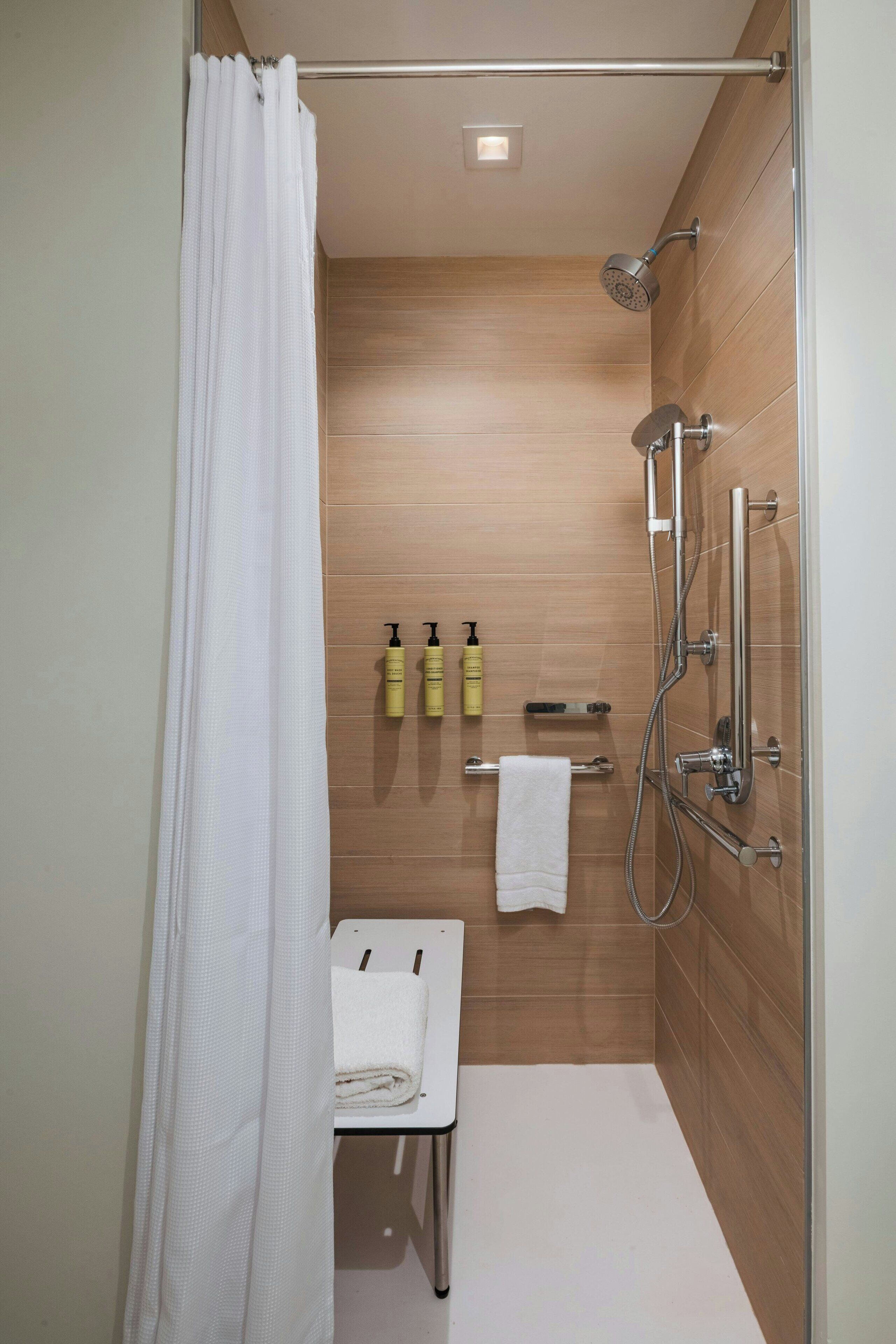 A modern shower with a handheld showerhead, a glass-enclosed shower stall, and a white towel on a small bench.