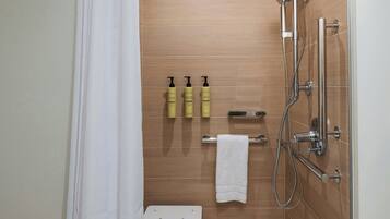 A modern shower with a handheld showerhead, a glass-enclosed shower stall, and a white towel on a small bench.