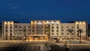 A multi-story hotel with a central entrance, parking lot, and a pool area with lounge chairs.
