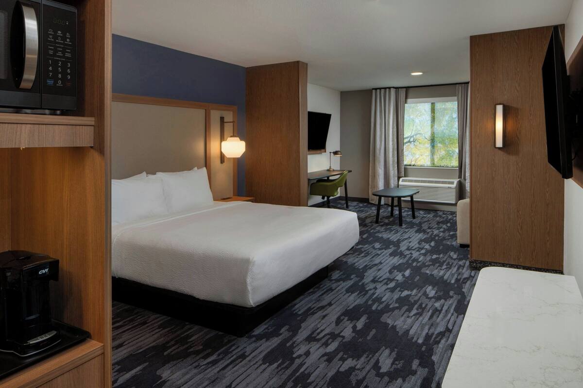 A hotel room with a large bed, a desk, a chair, a TV, and a coffee maker.