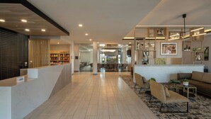 A modern hotel lobby with a reception desk, seating area, and a view into the dining area.