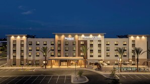A multi-story hotel with a central entrance, parking lot, and a swimming pool area. - Towneplace Suites By Marriott Surprise Prasada (Surprise)