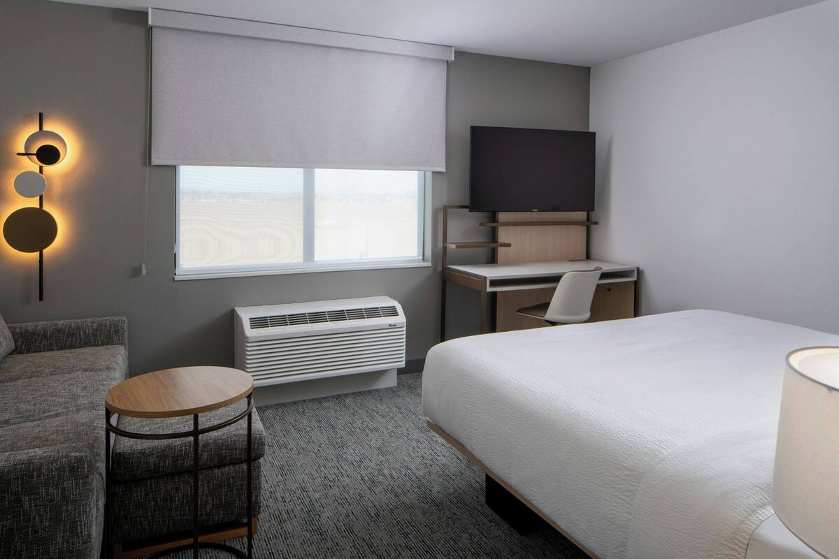 A hotel room with a bed, a desk with a TV, a sofa, a round table, and a wall-mounted air conditioner.