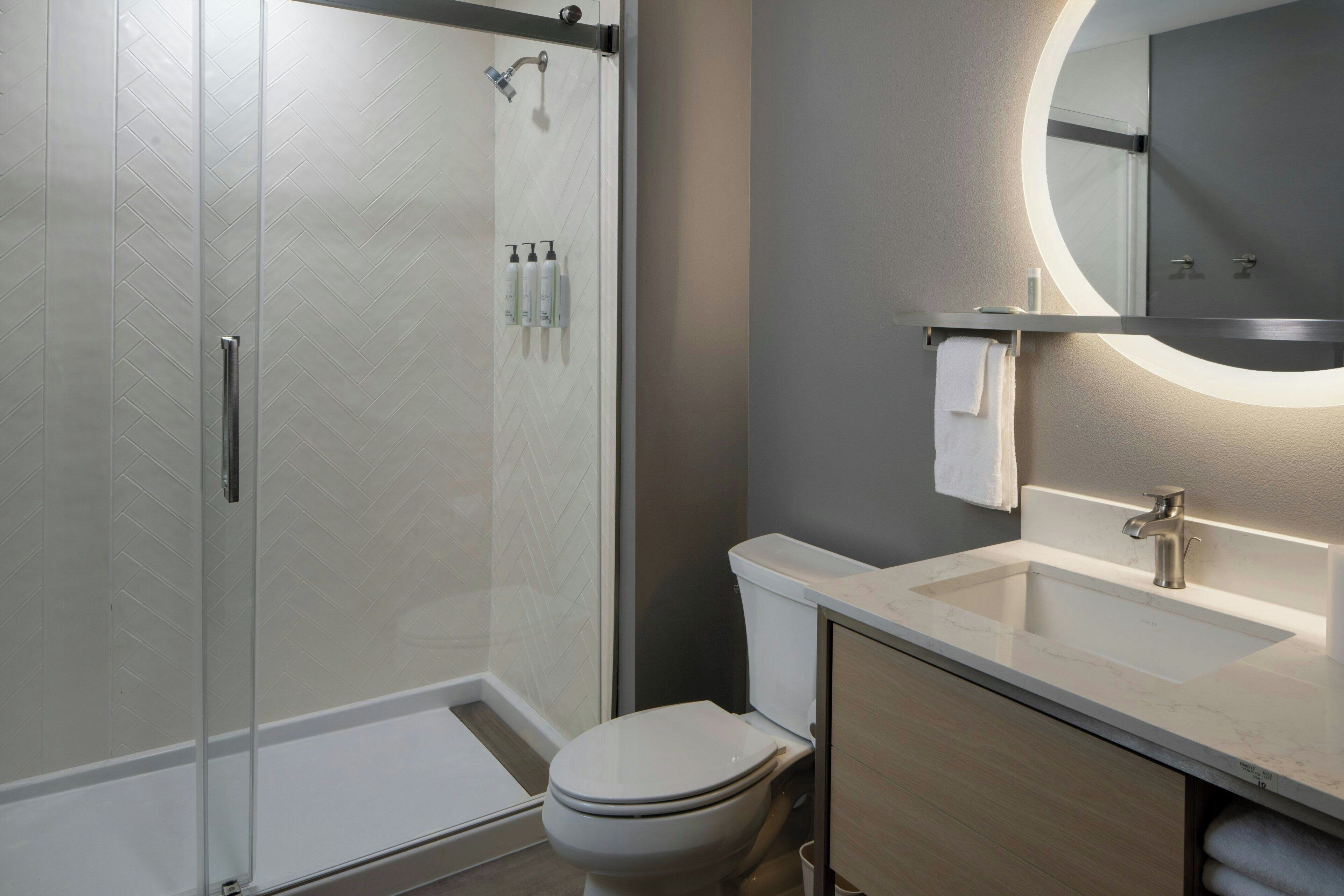 A modern bathroom with a glass-enclosed shower, a toilet, a sink with a mirror, and toiletries on the wall.