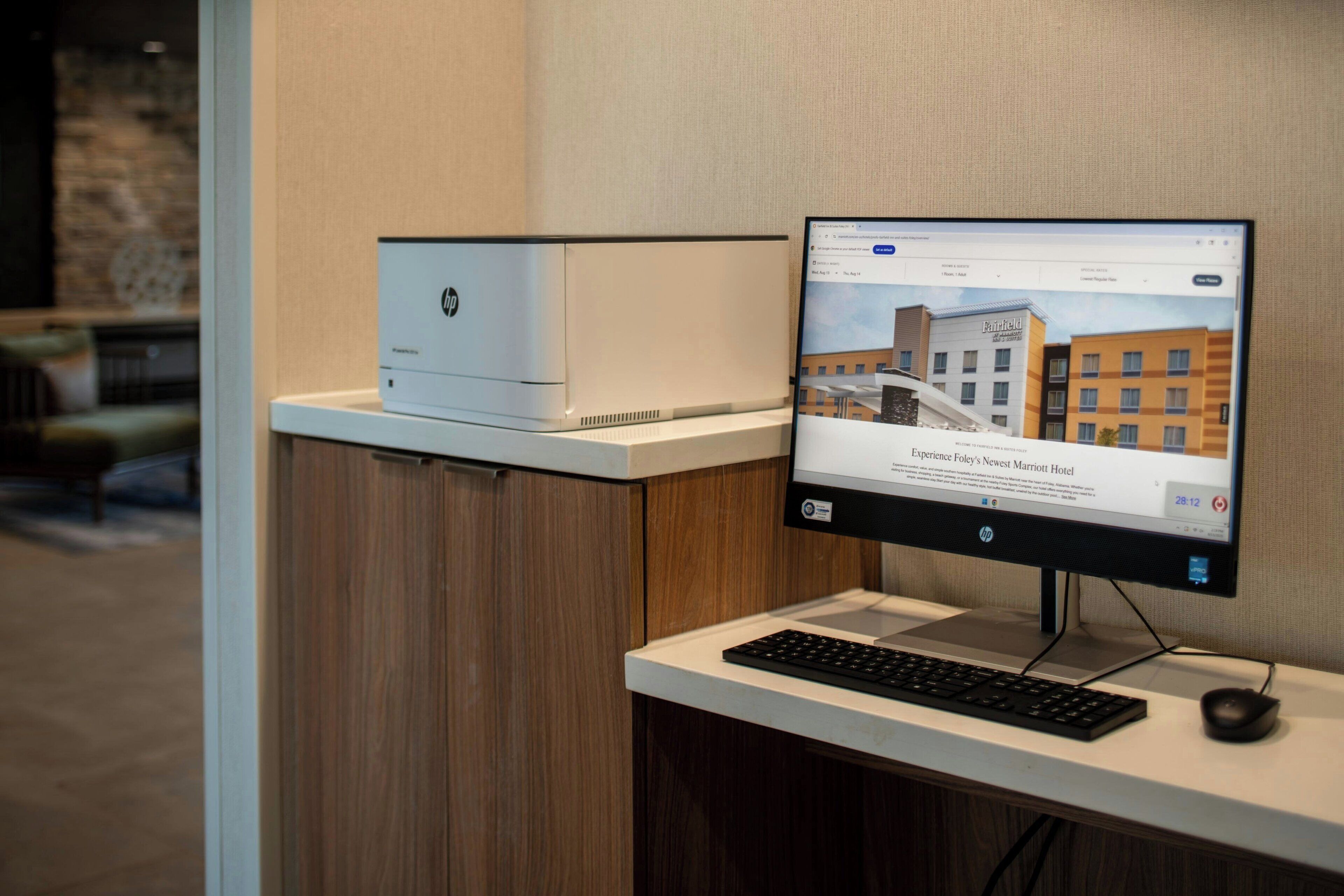 A computer monitor displaying a hotel website, a printer, and a keyboard on a desk.